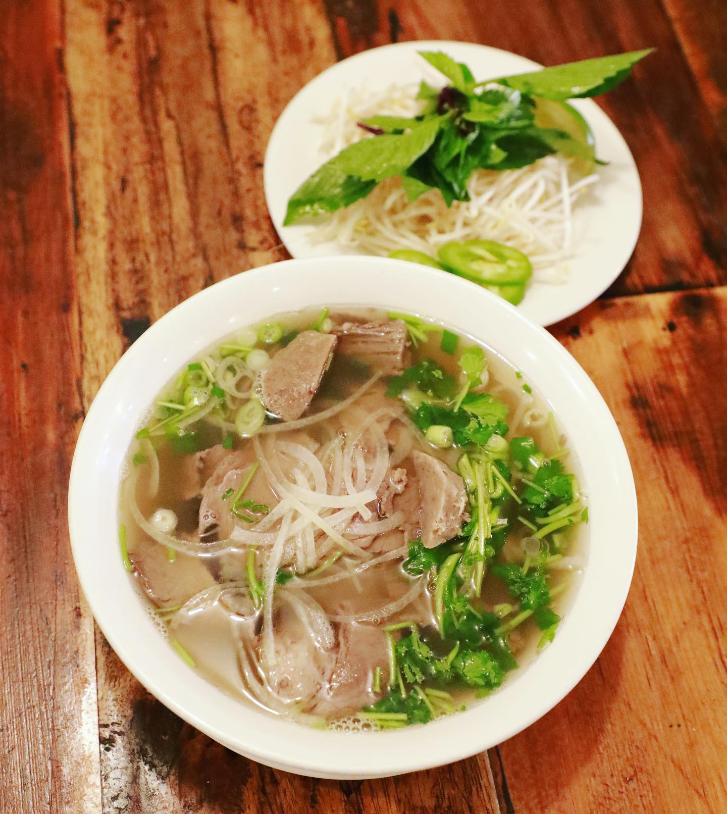 Bowl of traditional Vietnamese beef pho with clear broth, rice noodles, tender beef slices, fresh herbs, and garnish plate with bean sprouts and jalapeños at La Cà 38th in Tacoma